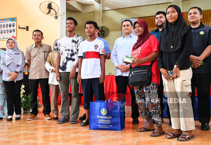 Mohd Arifin (tengah) menyampaikan bantuan TPNS kepada 18 pelajar mangsa kebakaran di Dewan SMK Usukan semalam.