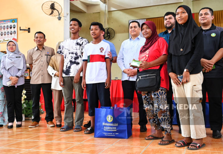 Mohd Arifin (tengah) menyampaikan bantuan TPNS kepada 18 pelajar mangsa kebakaran di Dewan SMK Usukan semalam.